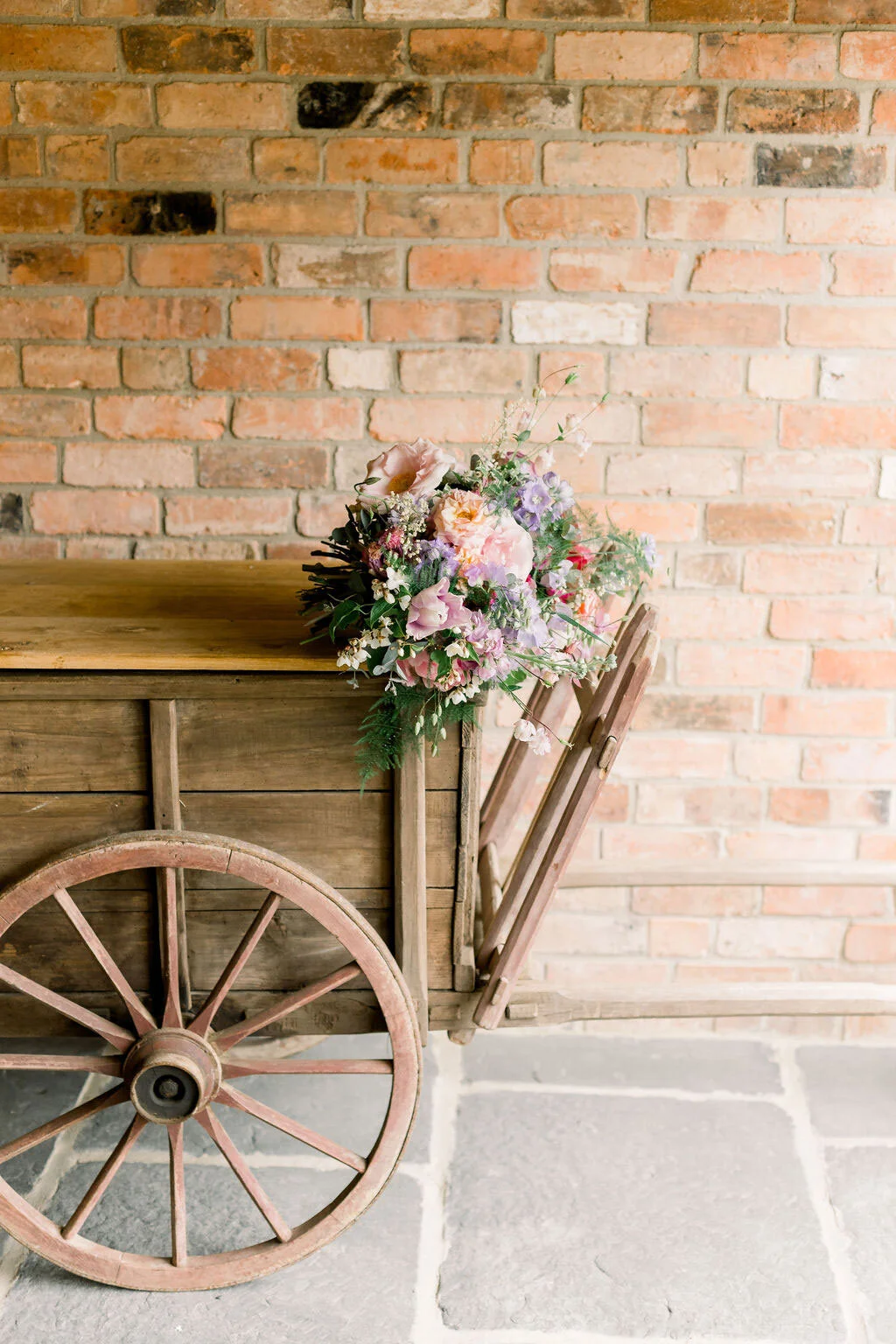 Wooden cart with bride's bouquet perched on top, against the bare brickwork of the barn
