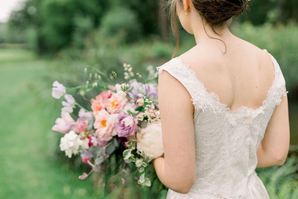Close up of the back of the bride and her bouquet walking alongside the lake