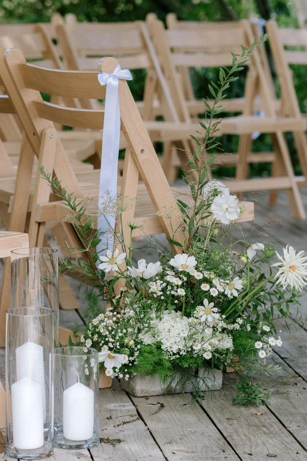 White and green cut flowers arranged at the end of the aisle with white candles in clear glass tall candle jars
