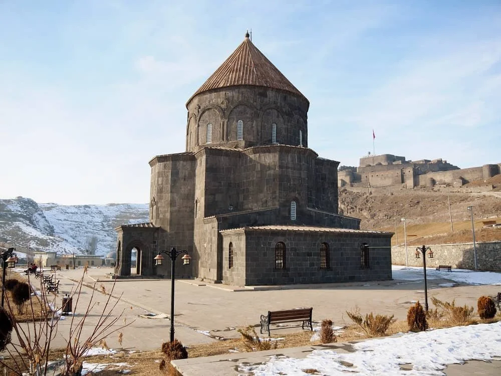 The Armenian style Kumbet mosque with a conical roof in Kars city centre with Kars castle in the background