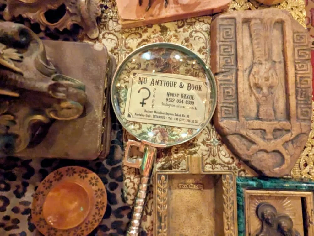 A magnifying glass sits on a business card for Nu Antik Cafe and Books surrounded by other antiques