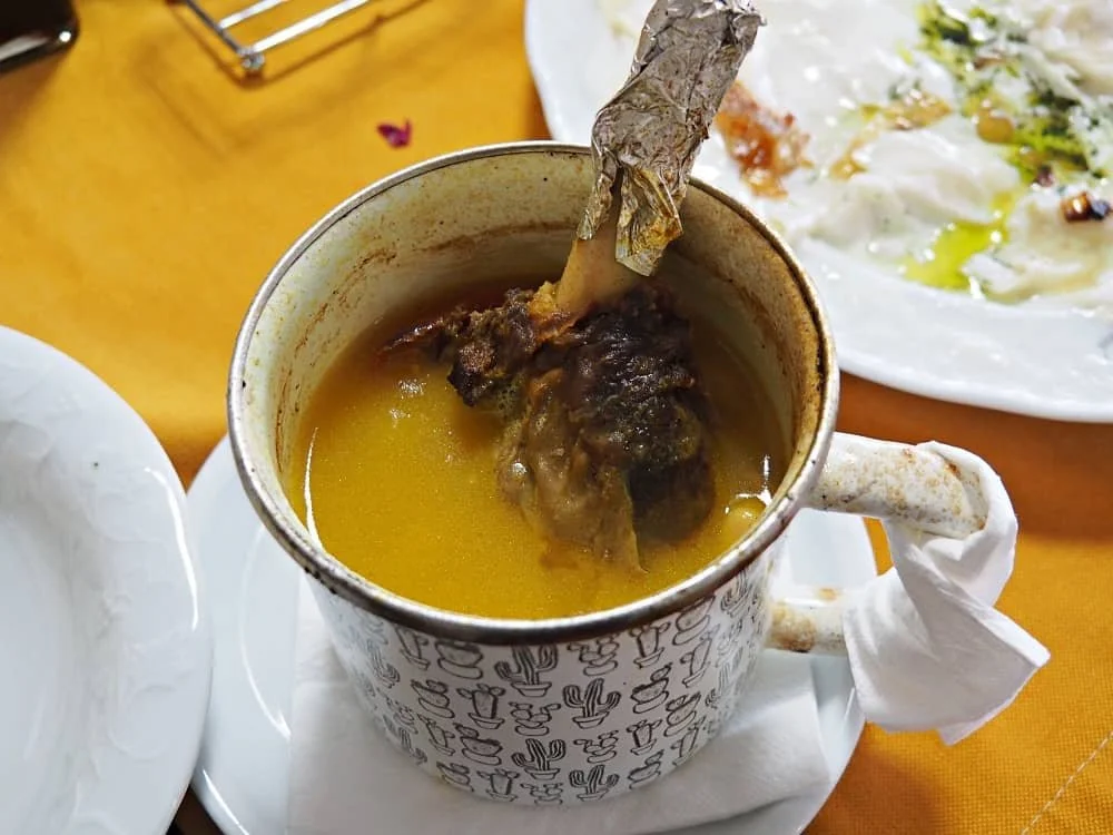 Image of piti, cooked lamb shank in an enamel mug with cooked chickpea stew
