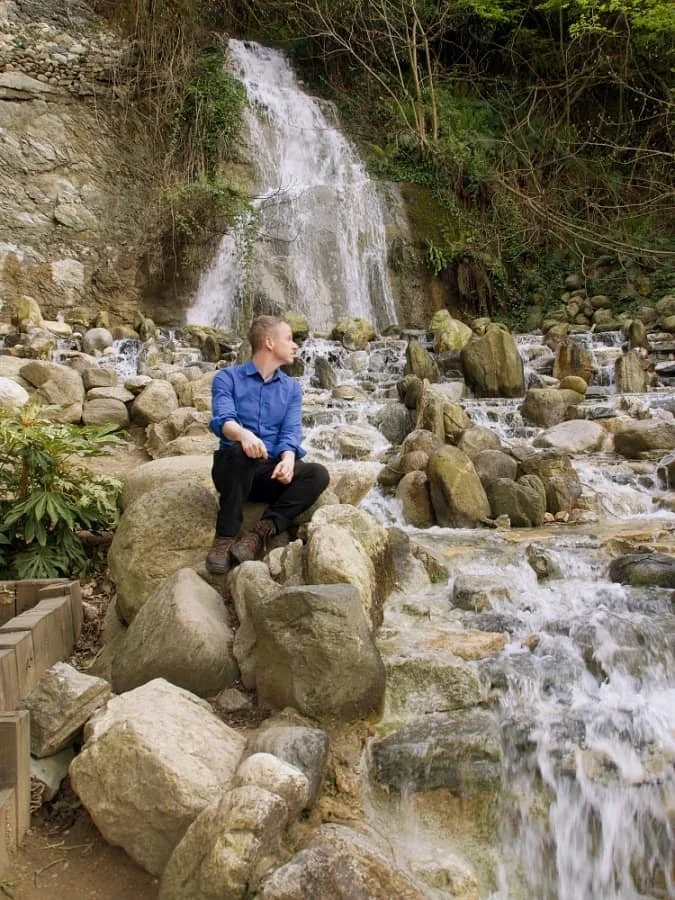 Vincent wearing a blue shirt and black trousers sits on some boulders looking at a waterfall in Hidiv Korusu in Kanlica, Beykoz, Istanbul