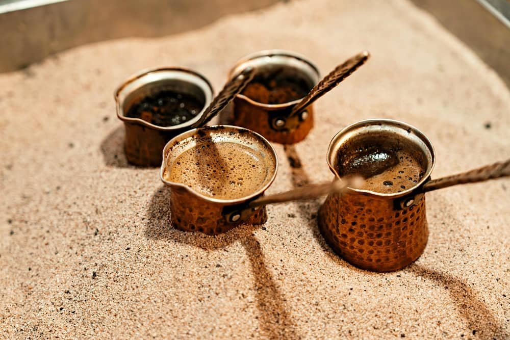Close up of copper Turkish cezves (coffee pots) cooking Turkish coffee on sand