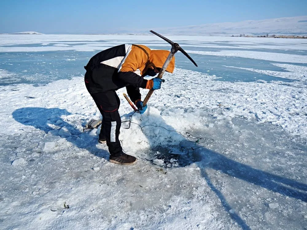 A fisherman uses a pickaxe to make a hole in the ice in order to pull out a net that he has placed beneath the ice on Lake Cildir in Kars in Turkey