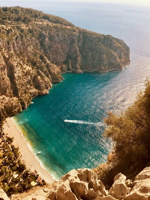 14 day travel itinerary turkey A small white strip of beach fringed by stunning aquamarine waters and towering sheer cliffs with a speed boat racing towards the bay at Butterfly Valley in Fethiye