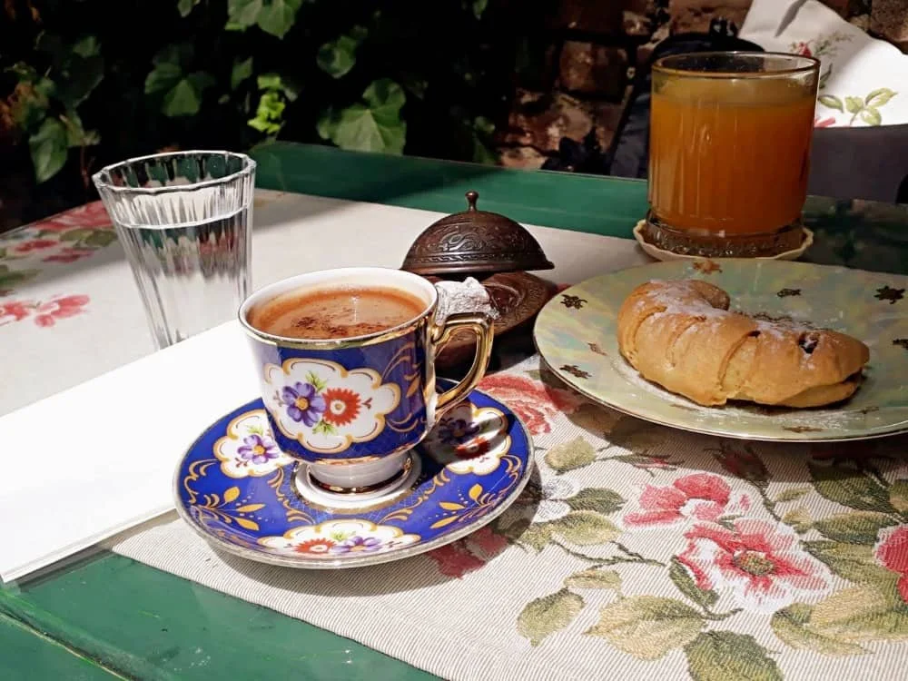 A Turkish coffee in a vintage flowered cup and saucer, next to an apple biscuit and a glass of orange juice at Velvet Cafe in Balat