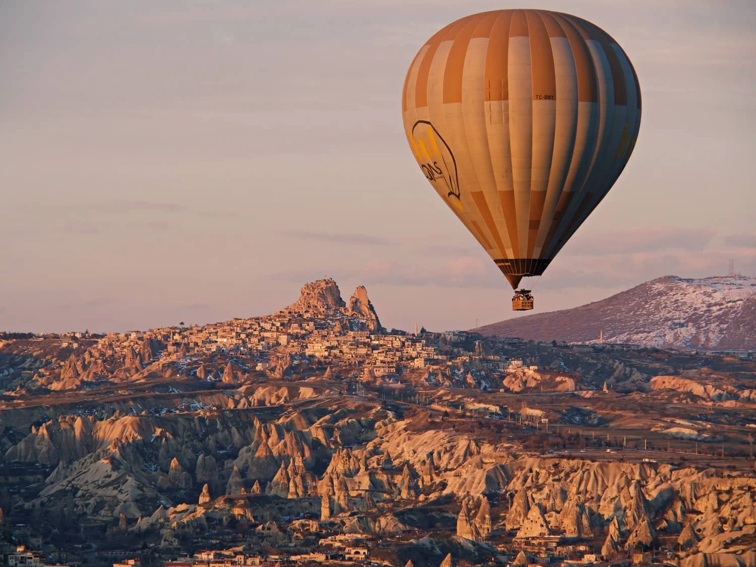 A hot air balloon flying over uchisar castle and town with fairy chimney rock formations in the foreground in Cappadocia