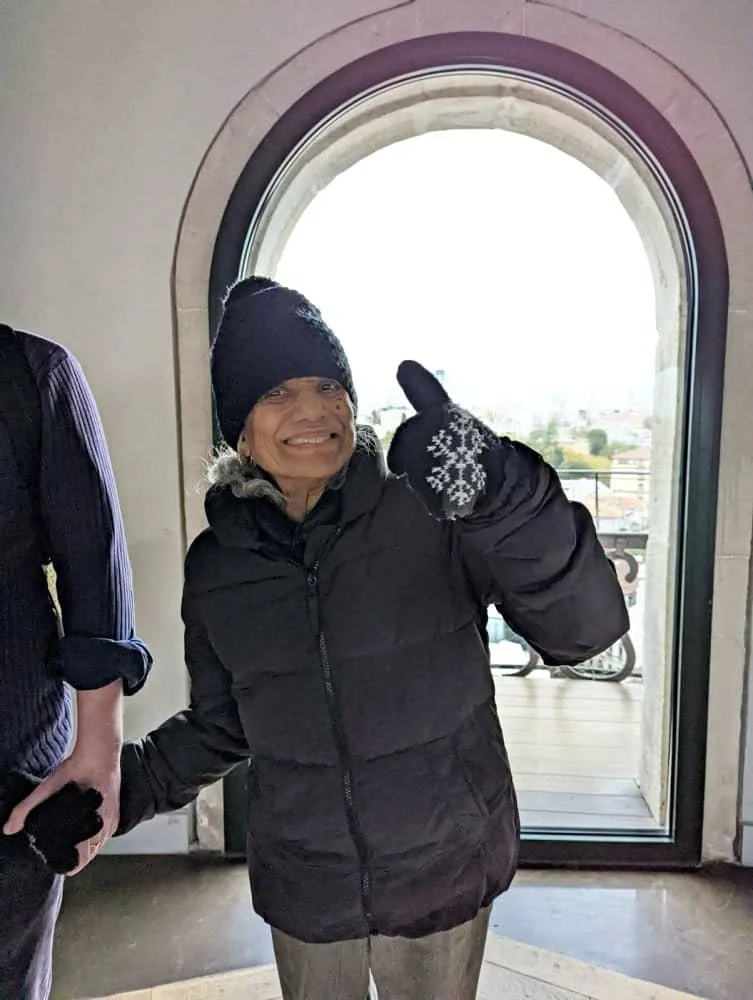 Sasha's mum wearing a black hat and puffer jacket gives a thumbs up at the top of the Galata Tower in Istanbul.