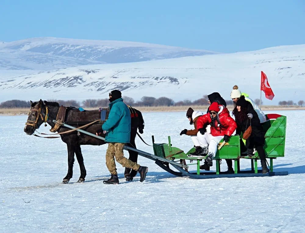 Tourists dressed in winter clothes get down from a bright green horse drawn sleigh on frozen Lake Cildir,  Kars turkey winter