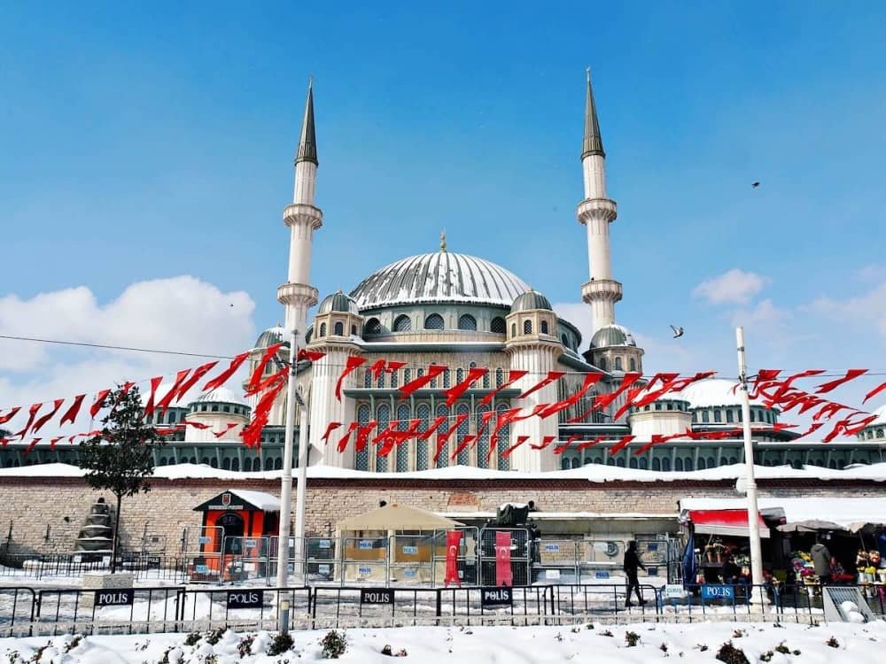 14 day travel itinerary turkey A layer of snow covers the newly built mosque in Taksim Square on a bright blue sky day. Red Turkish flags surround the mosque in Istanbul in TĂŒrkiye