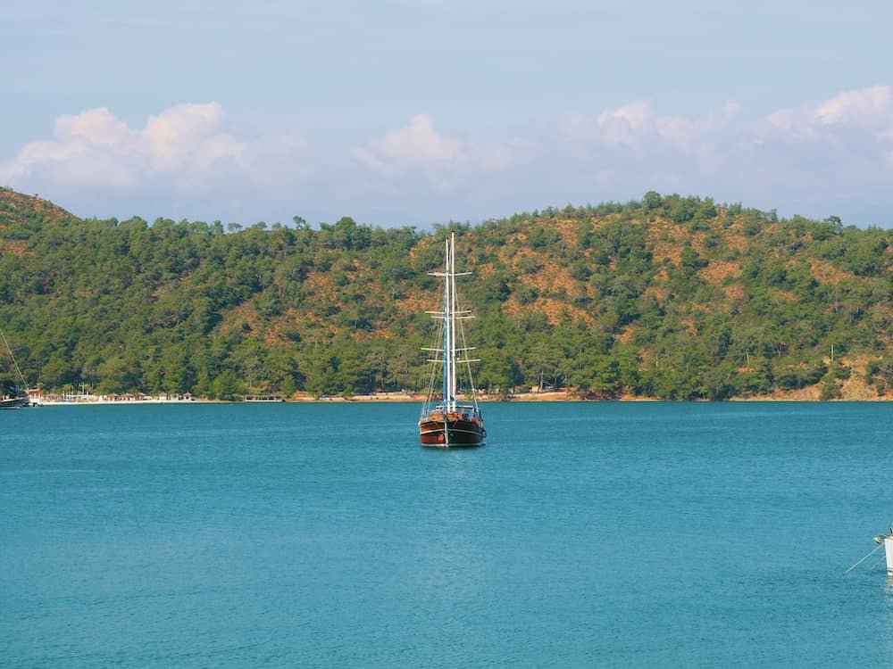 14 day travel itinerary turkey A small boat sailing on the blue sea with green forest covered hills in the background in Fethiye in TĂŒrkiye