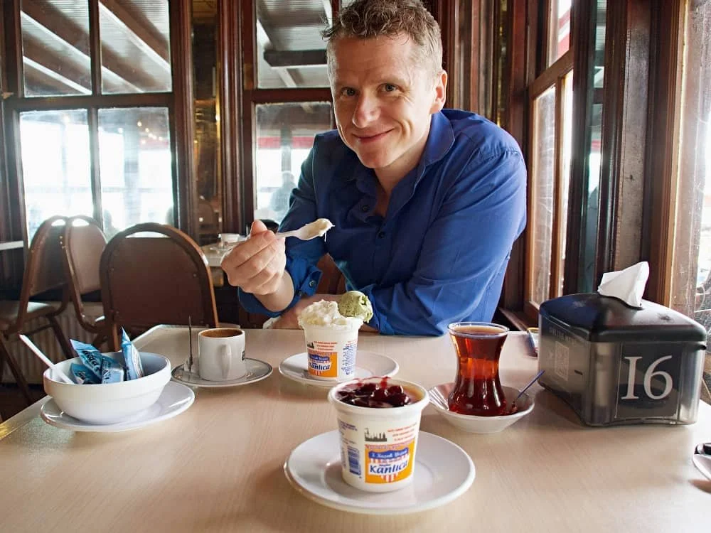 Vincent eating his kanlica yogurt with ice cream and in front of him is a pot of yogurt topped with cherry jam, a glass of tea and a cup of Turkish coffee.
