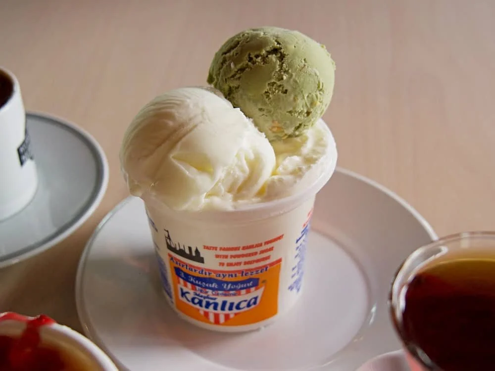 Close up of a pot of Kanlica yogurt topped with two scoops of pistachio and vanilla ice cream at Asirlik Kanlica Yogurdu in Kanlica