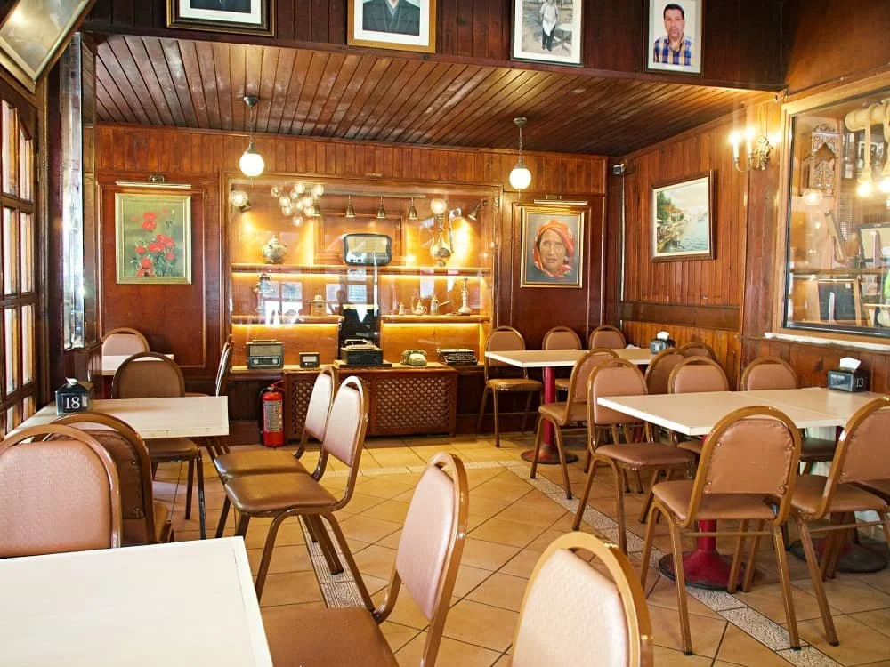 The wood panelled interior of kanlica asirlik cafe. There are antiques in a glass case in  the background and portrays of the owners of the cafe and creators of the yogurt on the walls.