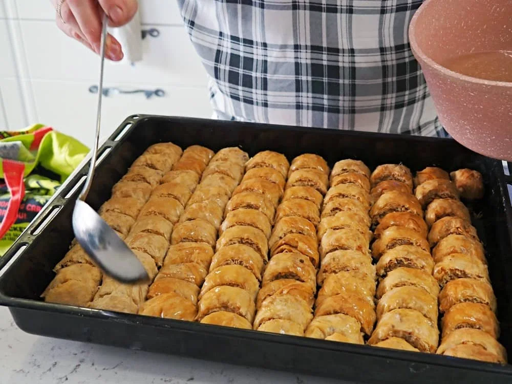 Syrup being poured onto a tray of golden just baked homemade baklava