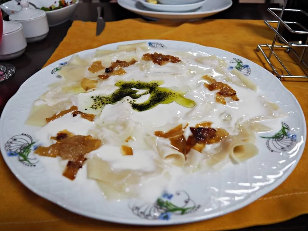 A plate of hingel - a thin pasta topped with garlic yogurt sauce, melted butter and caramelised onions