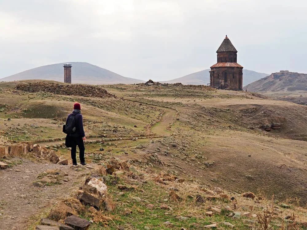 A man on a rocky path looking at the ruins of a church in the ani ruins kars turkey