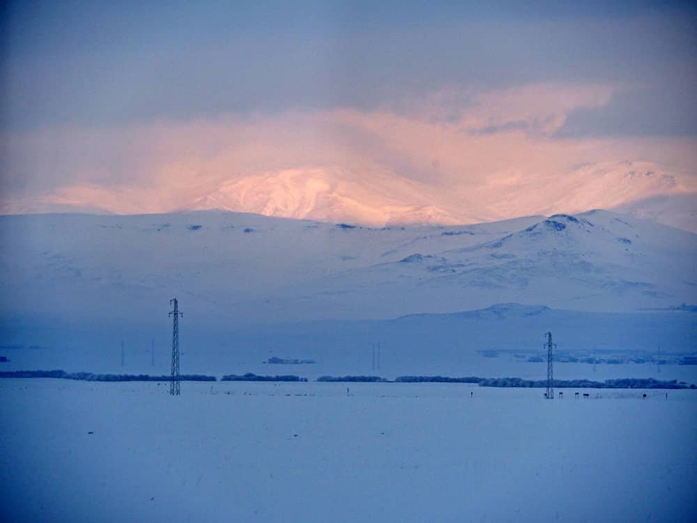 Snowy mountains lit up in pink by the rising sun as seen from the winndow of the Dogu Ekspresi train, train to kars