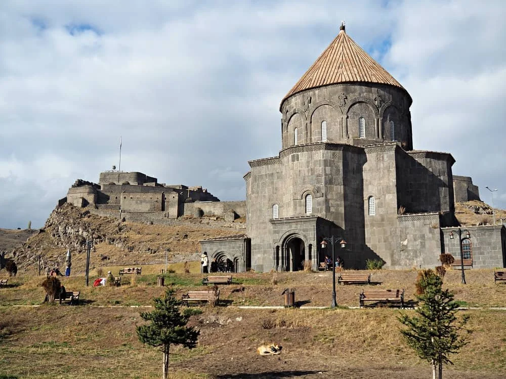 Close up of Kumbet Mosque with its distinctive cone shaped roof and with Kars castle in the background in the distance in Kars, Turkey