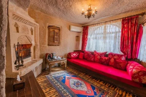 A beautifully furnished room with a large sofa, lit fireplace, Turkish rugs and a chandelier at Gamirasu Cave Hotel, 10 best hotels in cappadocia