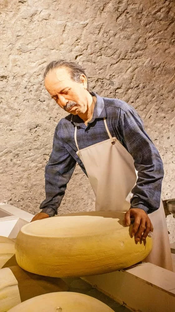A diorama showing a life size model of a man holding a finished cheese at the Kars Cheese Museum