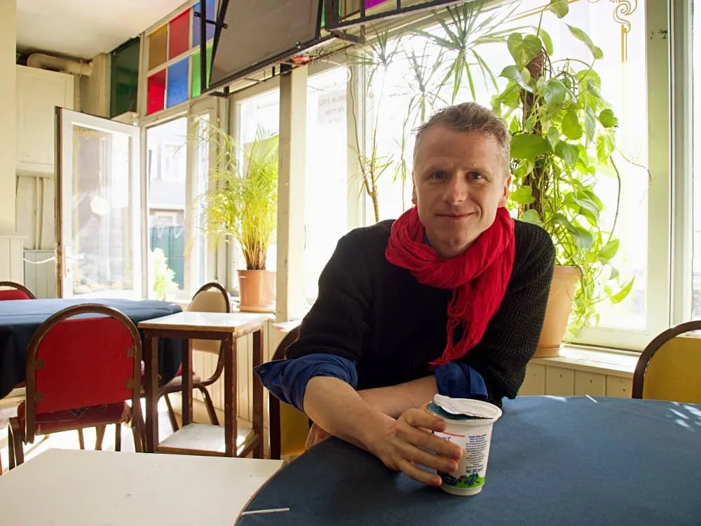 Vincent sits with an ayran in his hand at a local teahouse in Kanlica. A plant and a stained glass window decoration is behind him