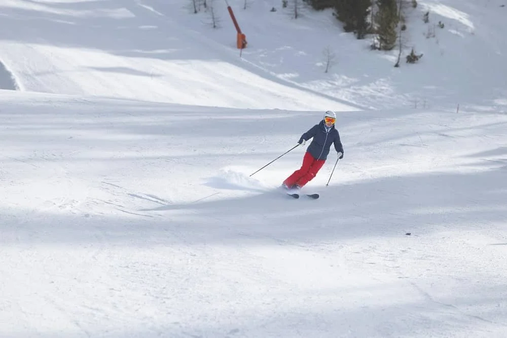 A person wearing a blue top, red trousers and colourful ski goggles skiing down a snow covered slope