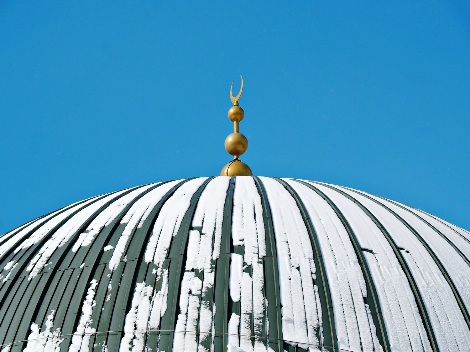 A close up of a dome of a mosque dusted in snow, with a bright blue sky behind, winter in istanbul 2023