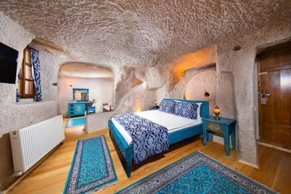 A bright cave room decorated with blue Turkish rugs and a blue bed runner at Portal Cappadocia Hotel, best hotel view in cappadocia