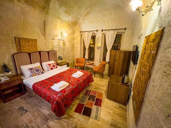 A spacious cave room with a large double bed, big windows with white drapes and a small seating area at Heritage Cave Suites, best view cave hotels in cappadocia