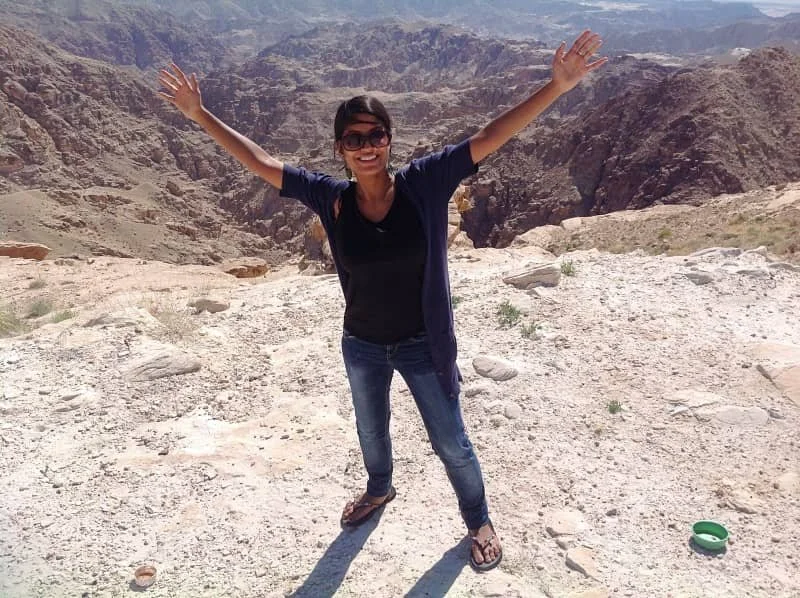 Sasha poses with her arms out wide on a steep cliff edge on the road to Petra in Jordan