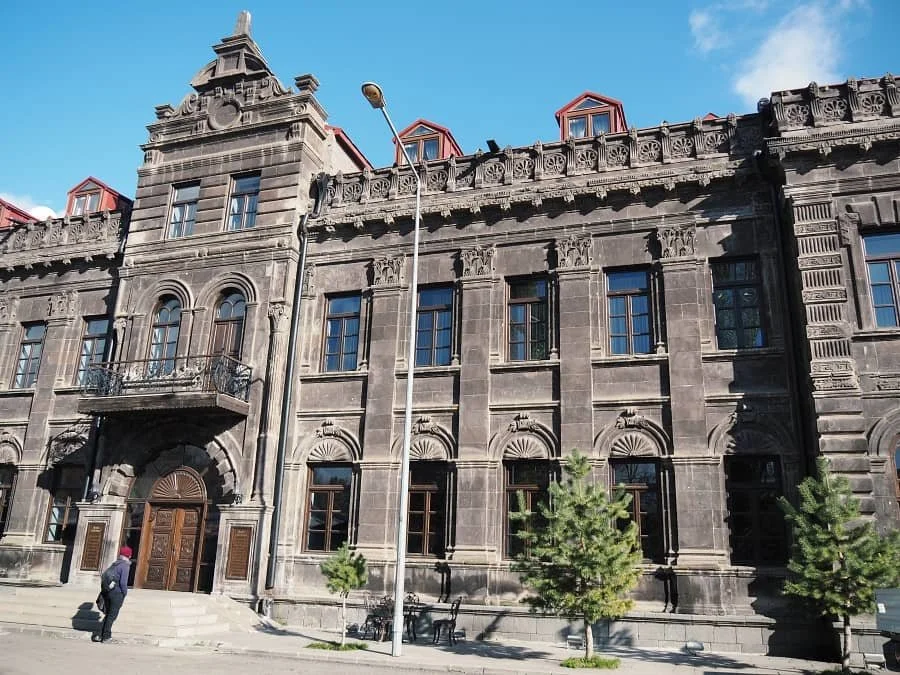 A man standing outside a Russian style grey stone building in Kars in Turkey