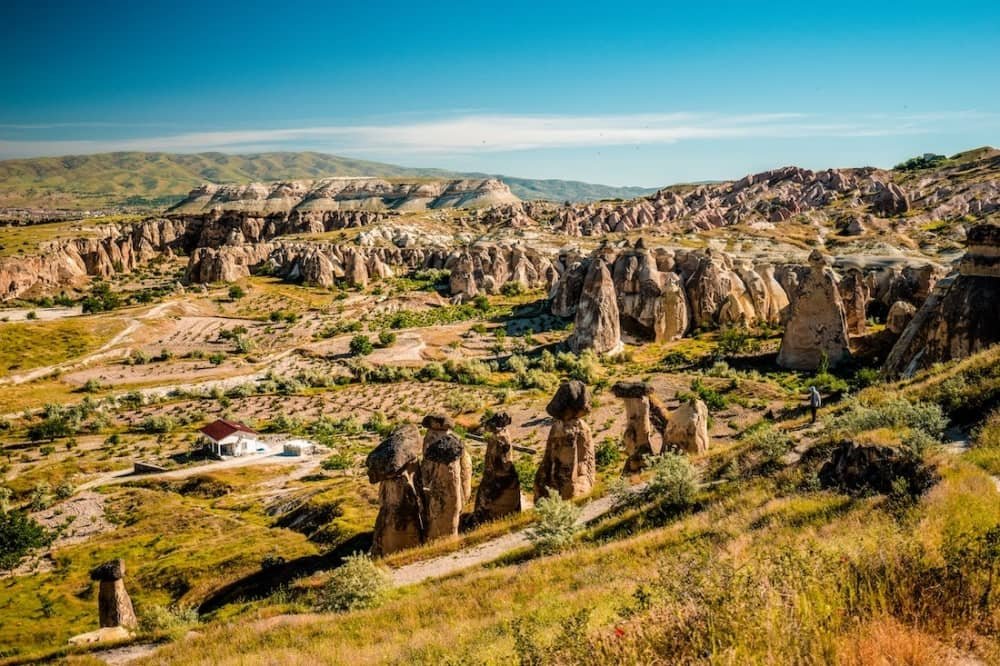 14 day travel itinerary turkey A single white house with a red roof sits in a green valley surrounded by fairy chimneys of all shapes and sizes against the backdrop of green mountains in Cappadocia in TĂŒrkiye