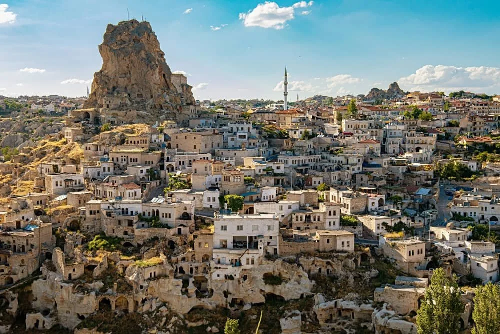 Ortahisar town with Ortahisar Castle towering in the background on a sunny day with a blue sky, which area to stay in cappadocia