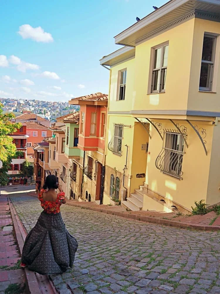 A woman in a long skirt and Spanish-style top takes a photo of the coloured houses in Istanbul