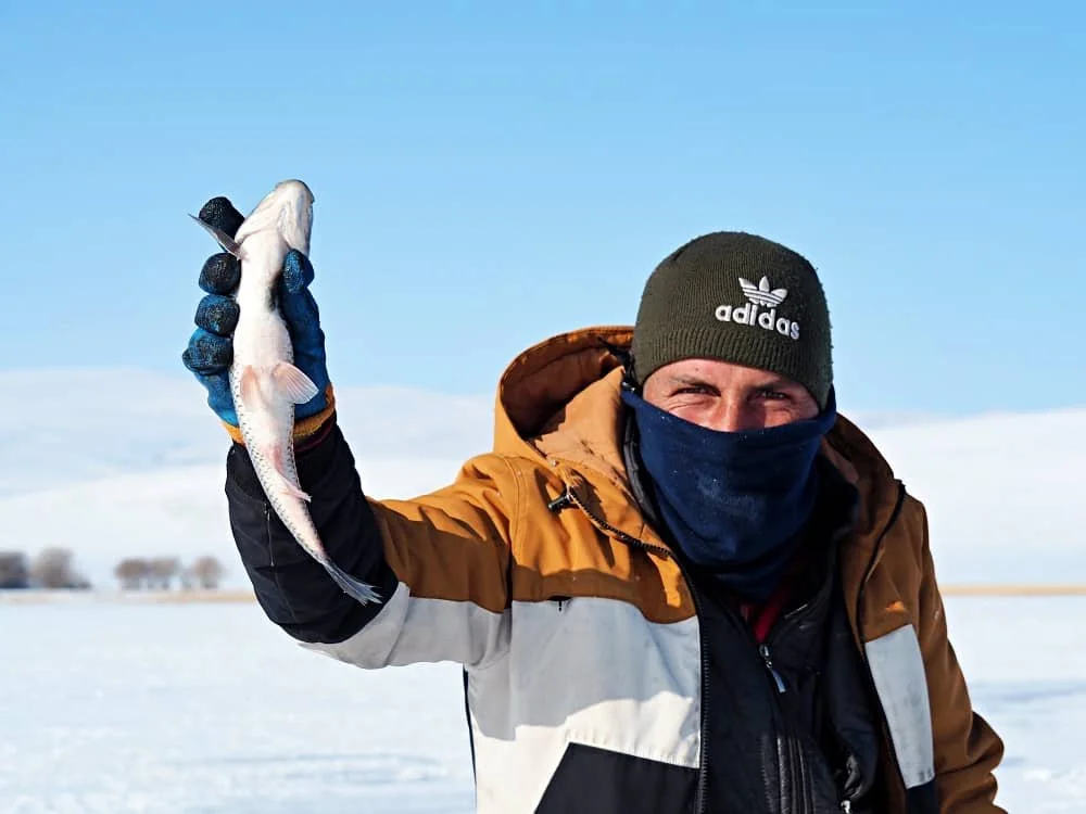 A fisherman holds up a fish he has just removed from a net beneath the ice on Lake Cildir in Kars in Turkey