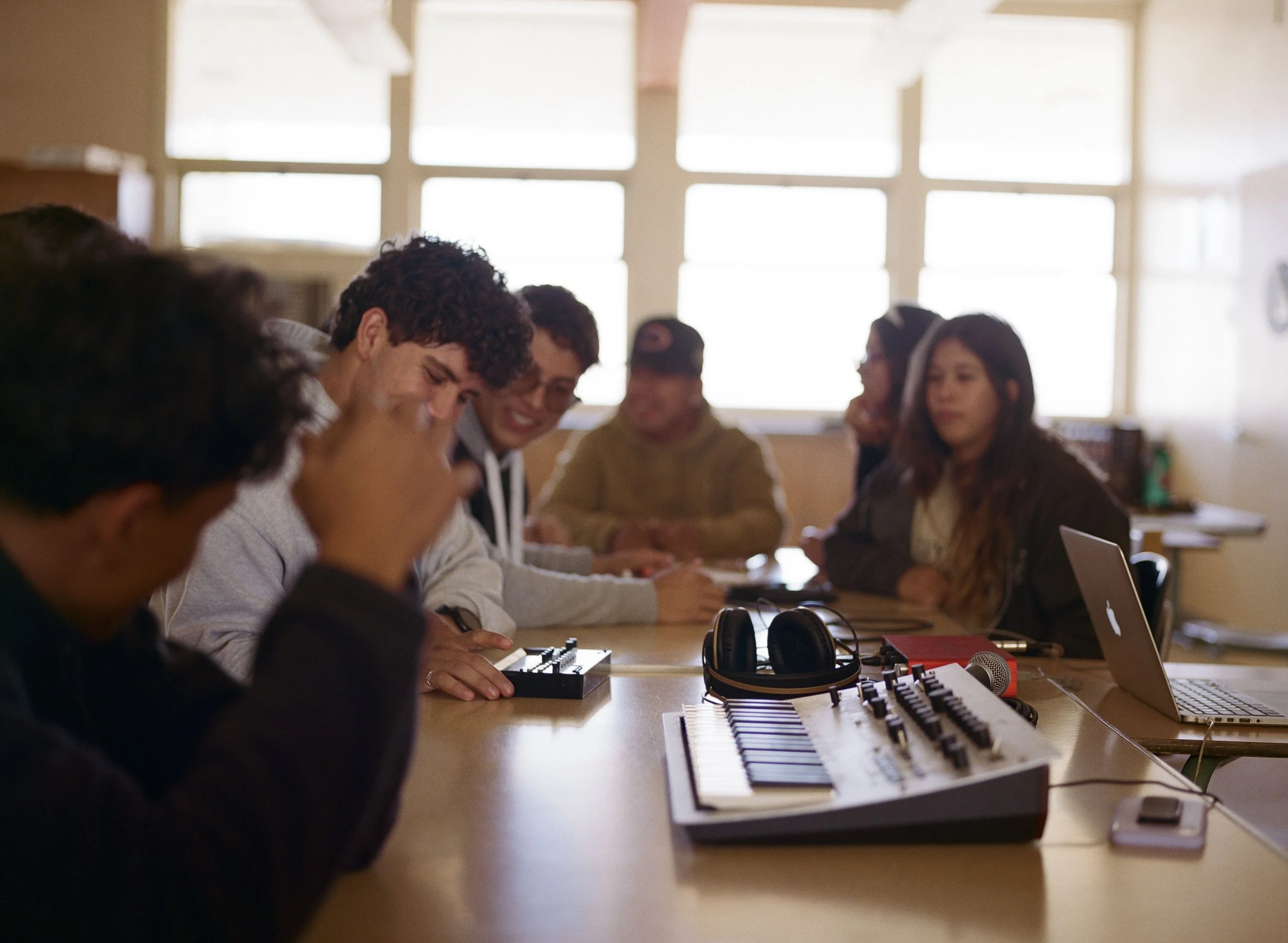 Cuyama students sit at a table and listen to music, a synthesizer and headphones are on the table.