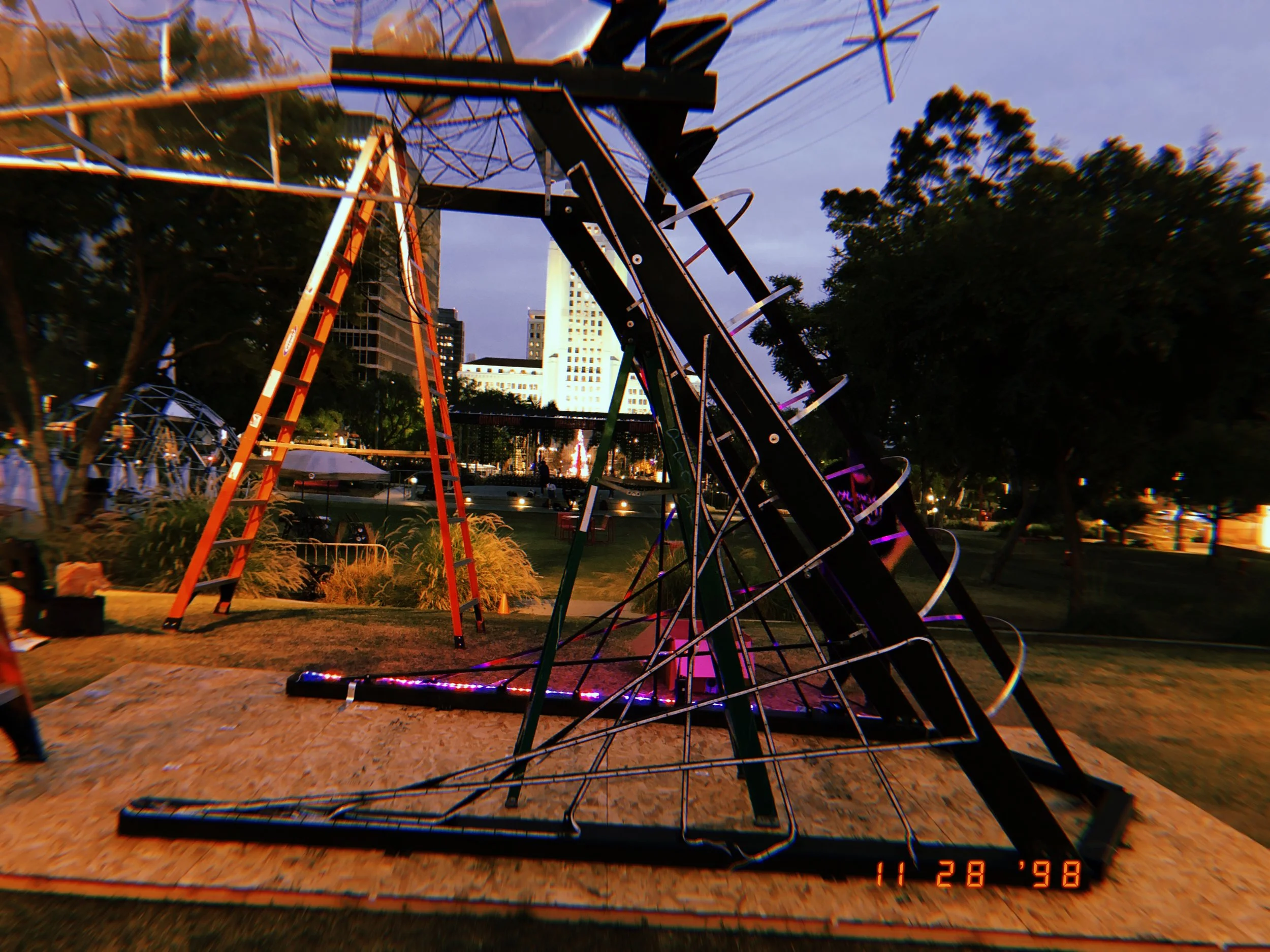 A locked roller coaster at a park during twilight, with trees and city buildings in the background.