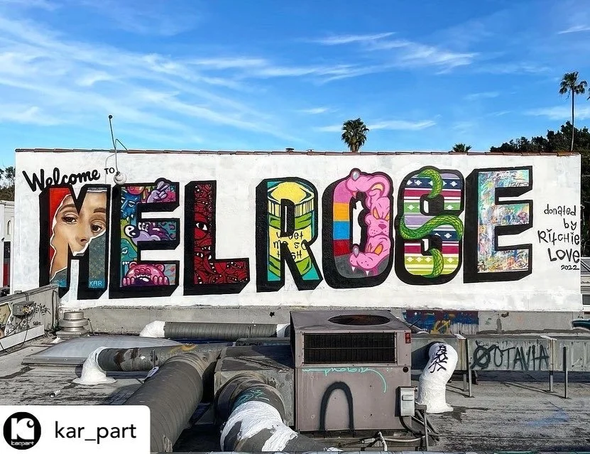 Colorful graffiti mural on a white wall spelling out 'HELLOISE' with artistic designs inside the letters, and a small portrait of a woman’s face on the left side. The mural is signed by Ritchie Love 2022.