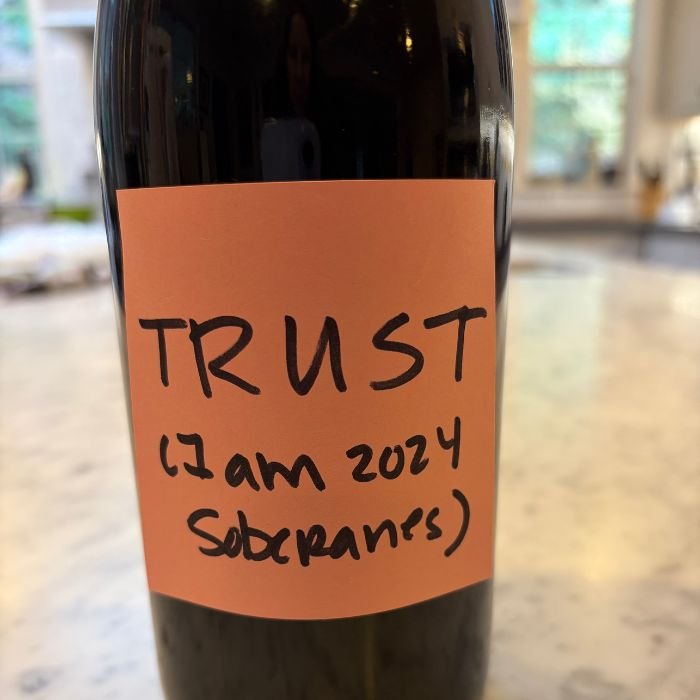 wine bottle with a paper hand written label that says "trust"