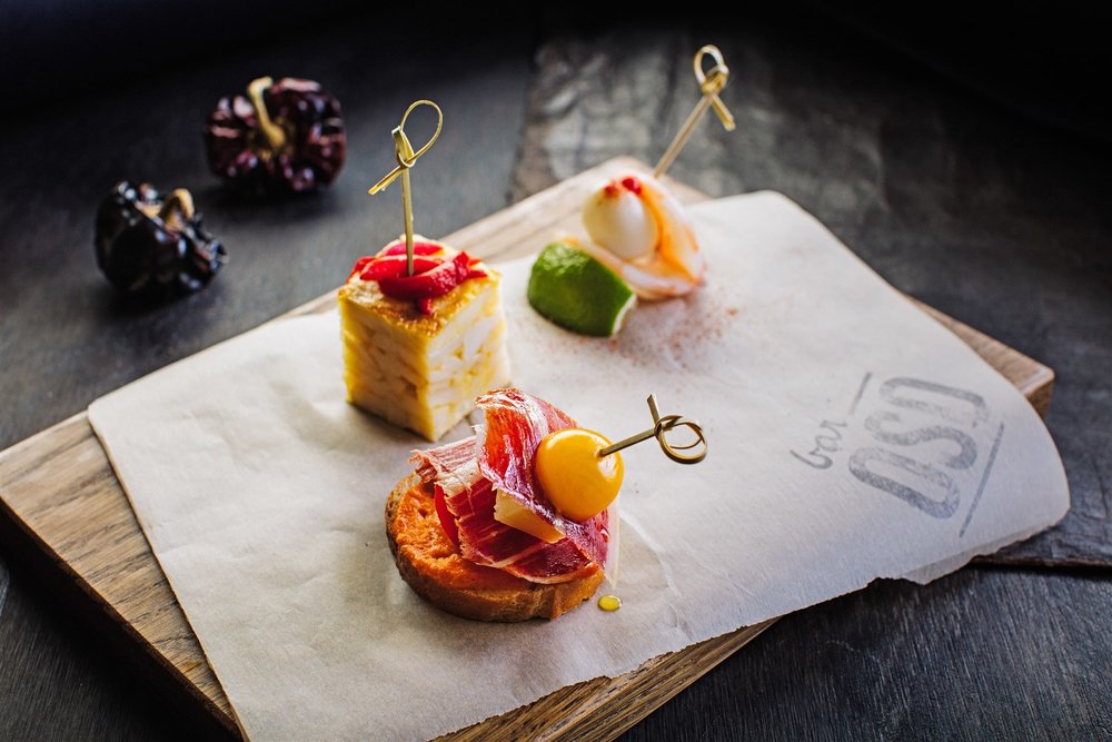  Pintxos—bites of flavors like  Bar Oso 's iberico ham, manchego cheese and tomato skewered together with a piece of bread—are classic Basque bar food.  Kevin Clark | Courtesy Toptable Group  