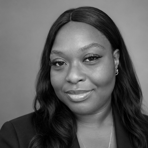 Black and white portrait of a woman with long dark hair, wearing a blazer and necklace, smiling softly at the camera.