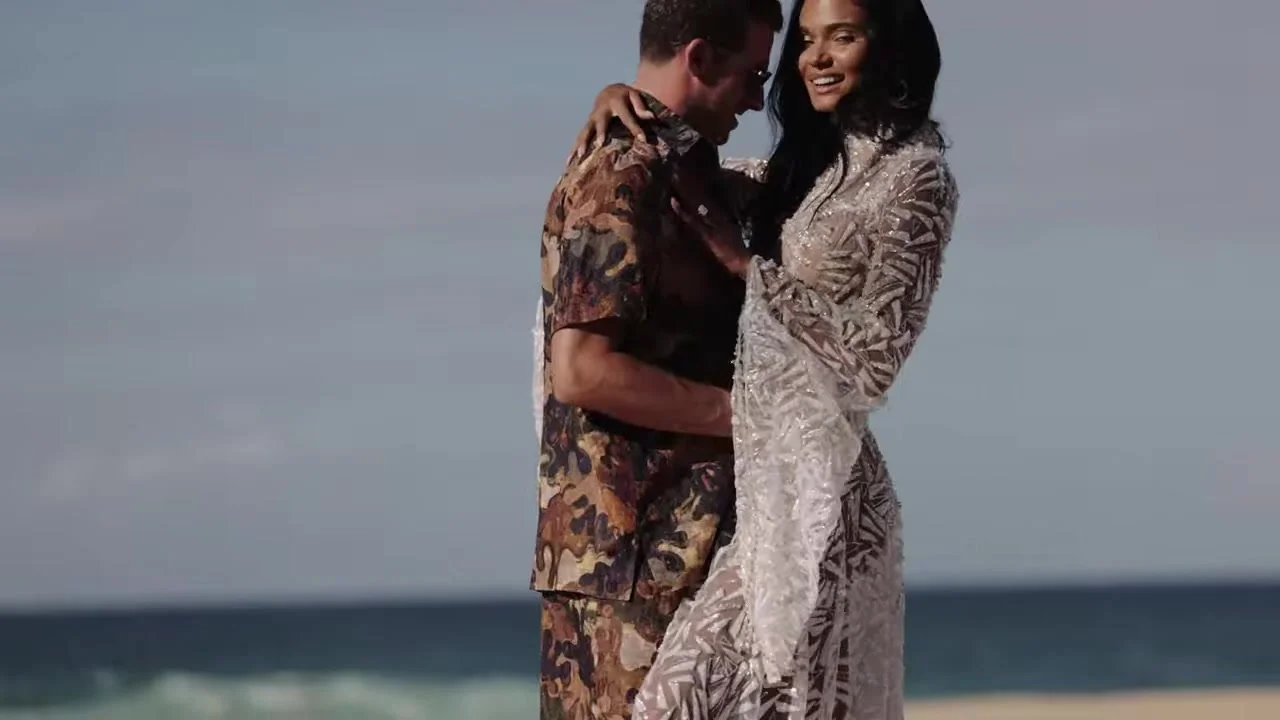 Daniela and Adam on the sand, her embroidered gown against turquoise water