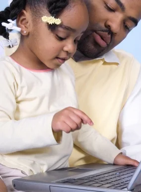 Dad and little girl finding letters on a laptop; print knowledge, a pre-reading skill, is important for reading success. Find out more at Canto Speech Therapy Online