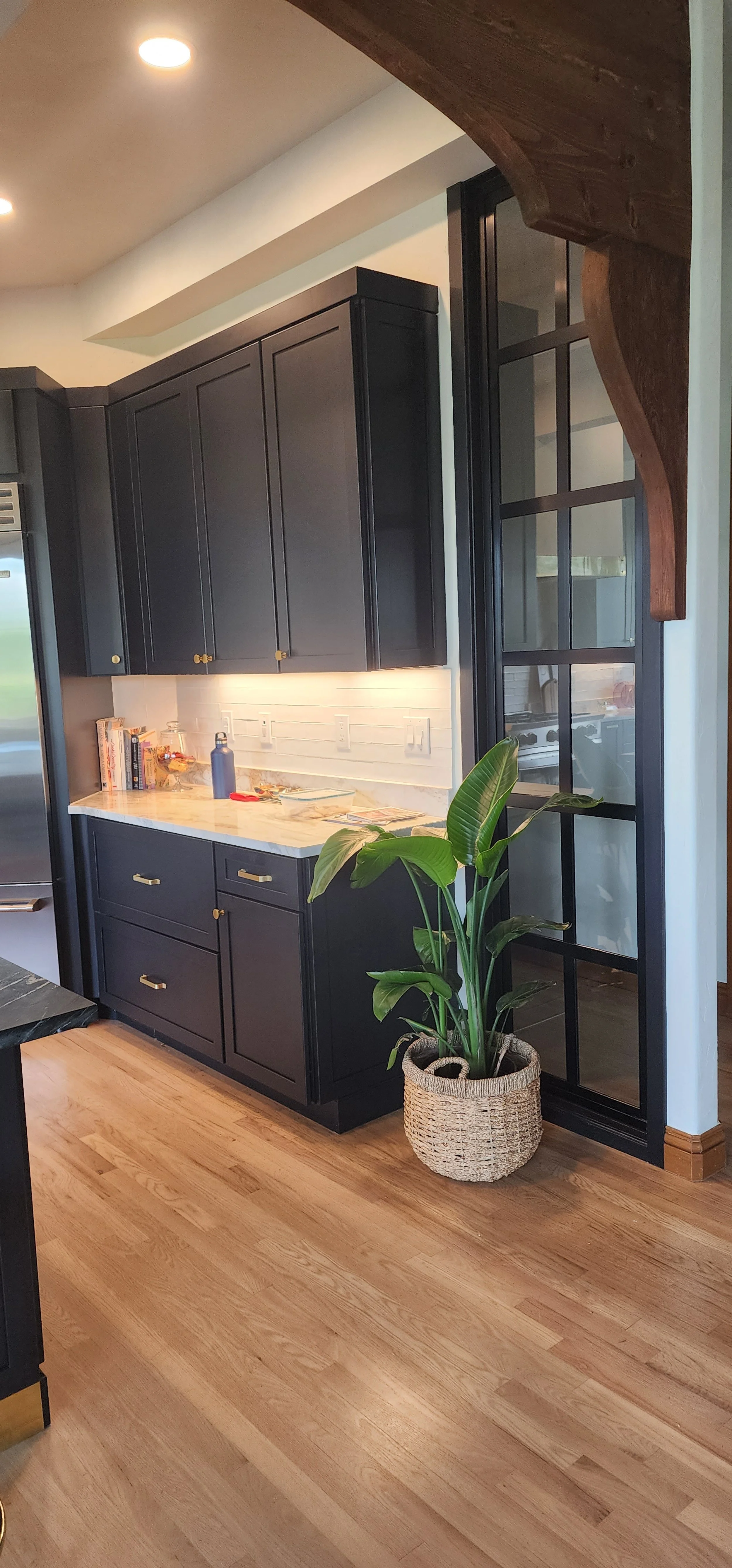 Kitchen with black cabinets, white backsplash, wooden floor, and glass sidelight.