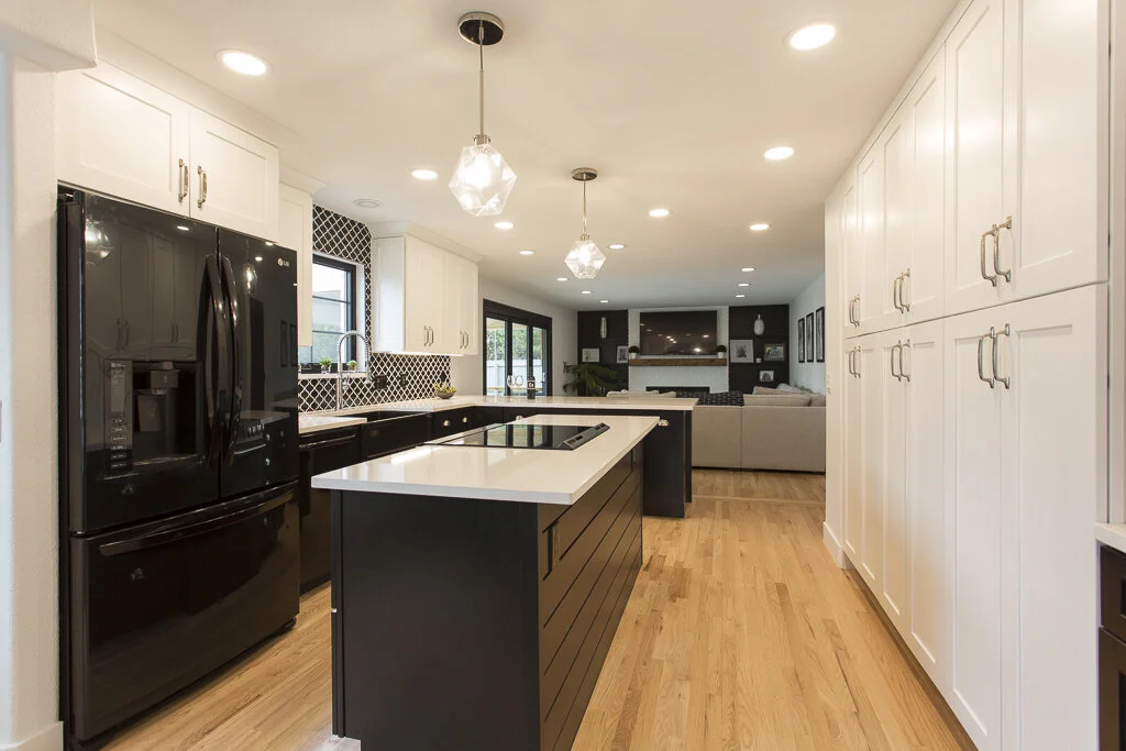 Modern kitchen with black & white cabinets with white countertop, hardwood floors, and pendant lighting.