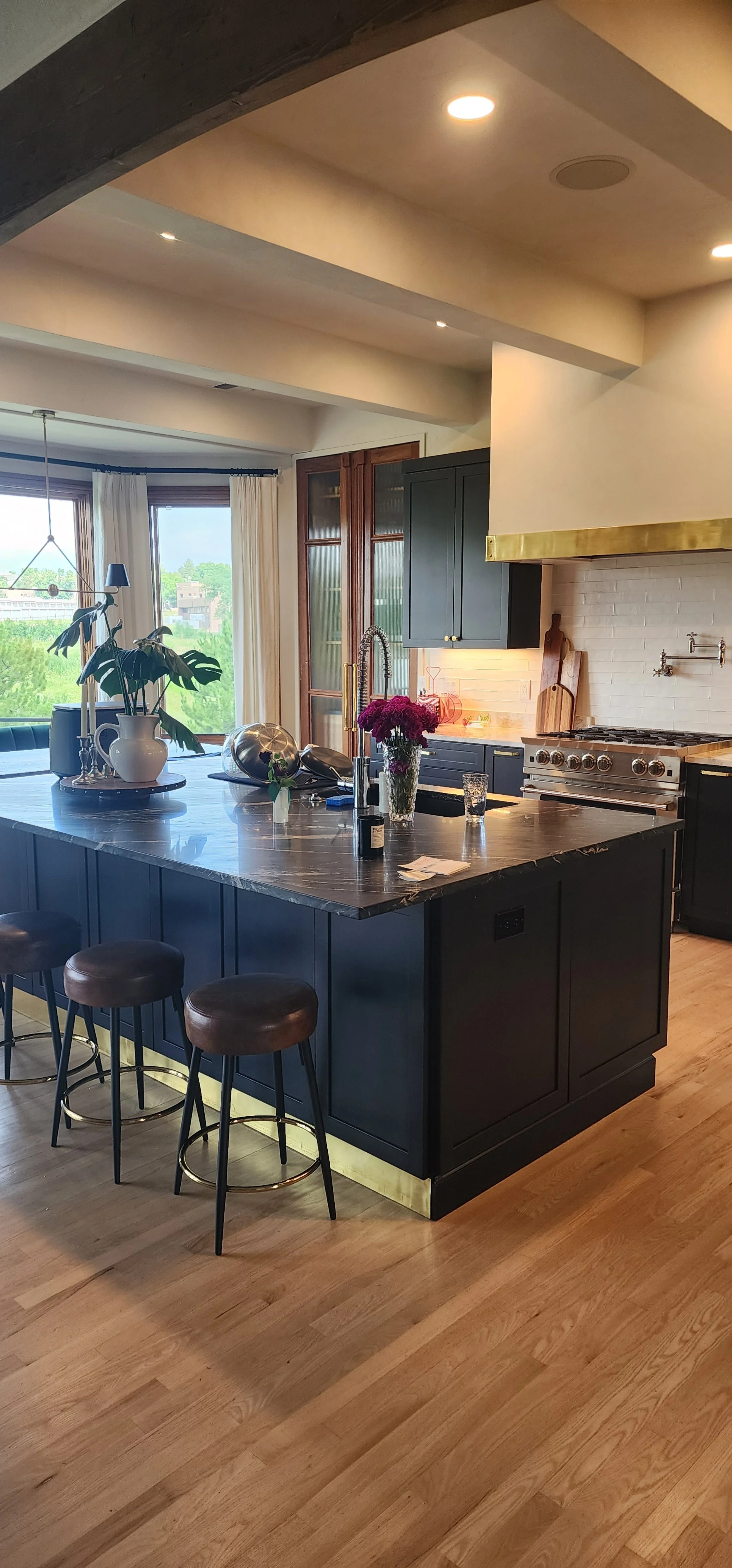 Modern kitchen with black cabinets, a large island with stool seating, a stove, and a window with a view of the outside.