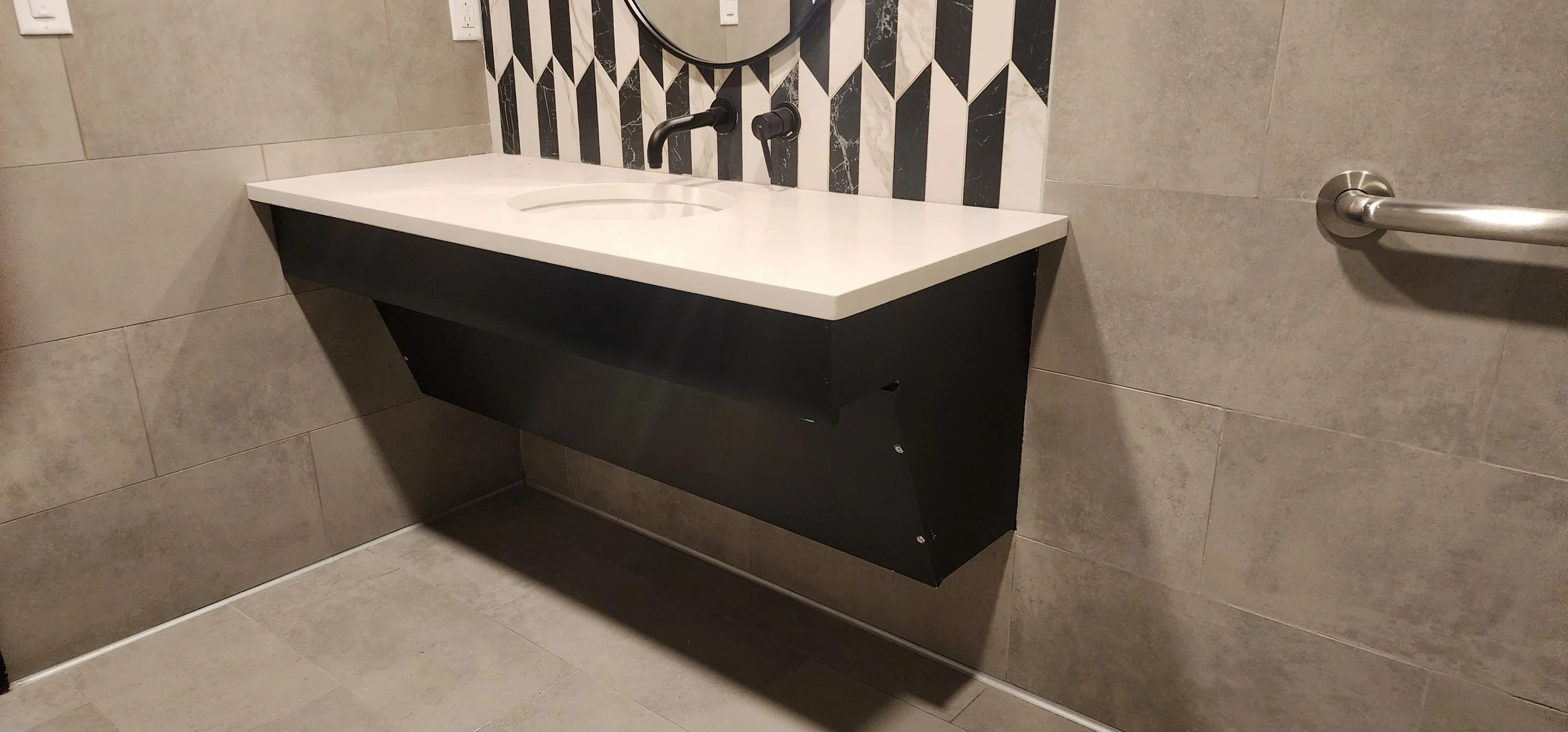 Modern bathroom with a floating Greenblack vanity, white countertop, oval sink, black wall-mounted faucet, and a circular mirror above the sink.