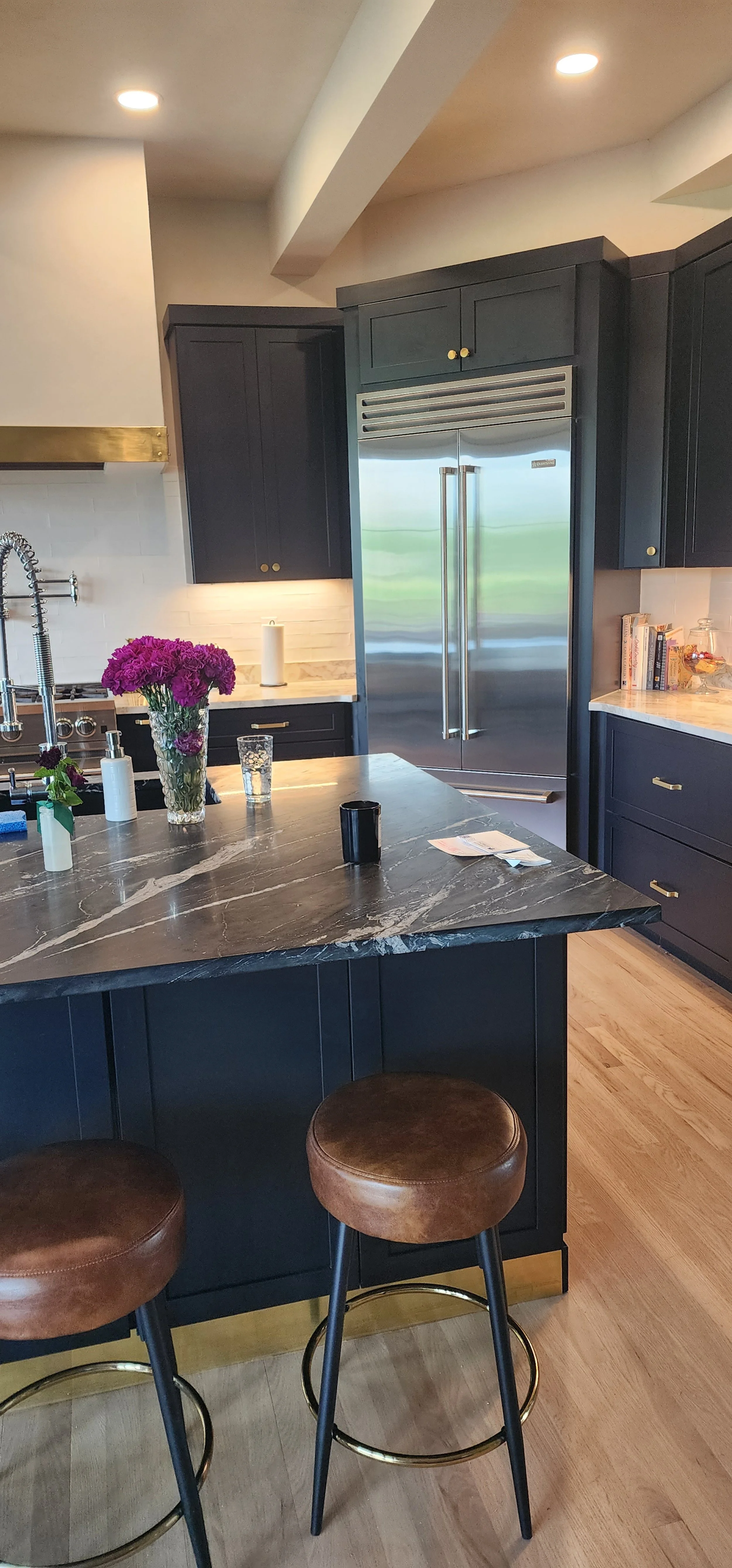 A modern kitchen with dark cabinets, a stone island with bar stools, and stainless-steel appliances.